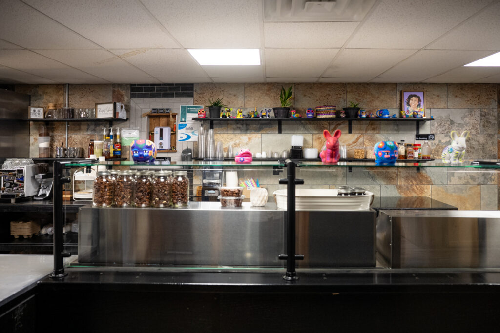 Shelves of jars, coffee supplies, and bright ceramic figurines decorate El ArteSano’s counter, blending Mexican folk art with a modern workspace.