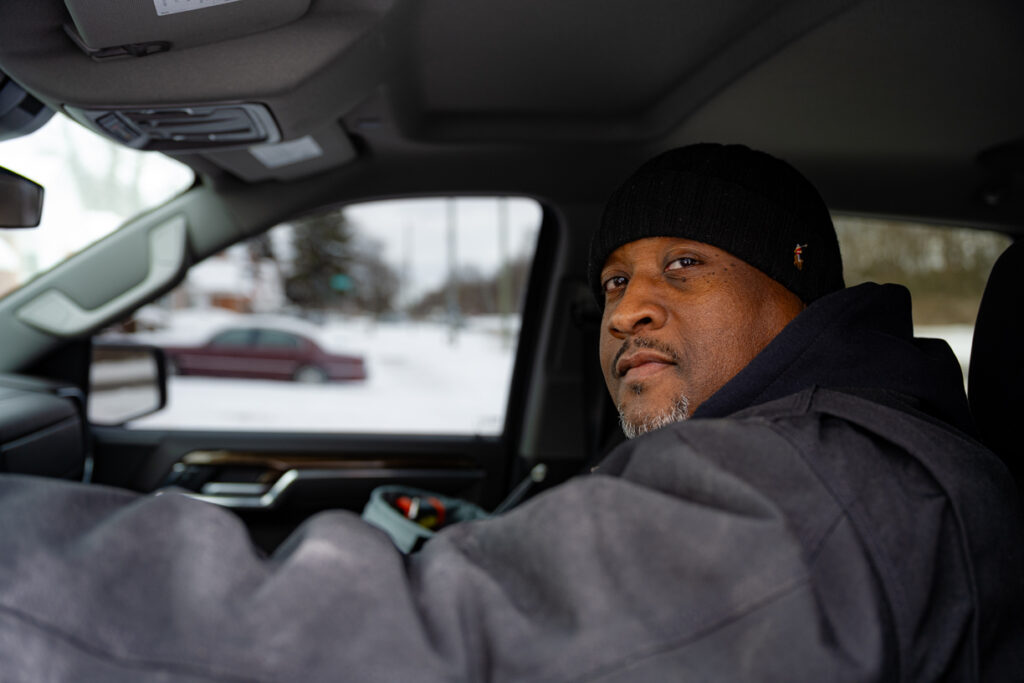 Gary Ringer sits in a truck during winter, looking back toward the camera, snow visible outside the window.