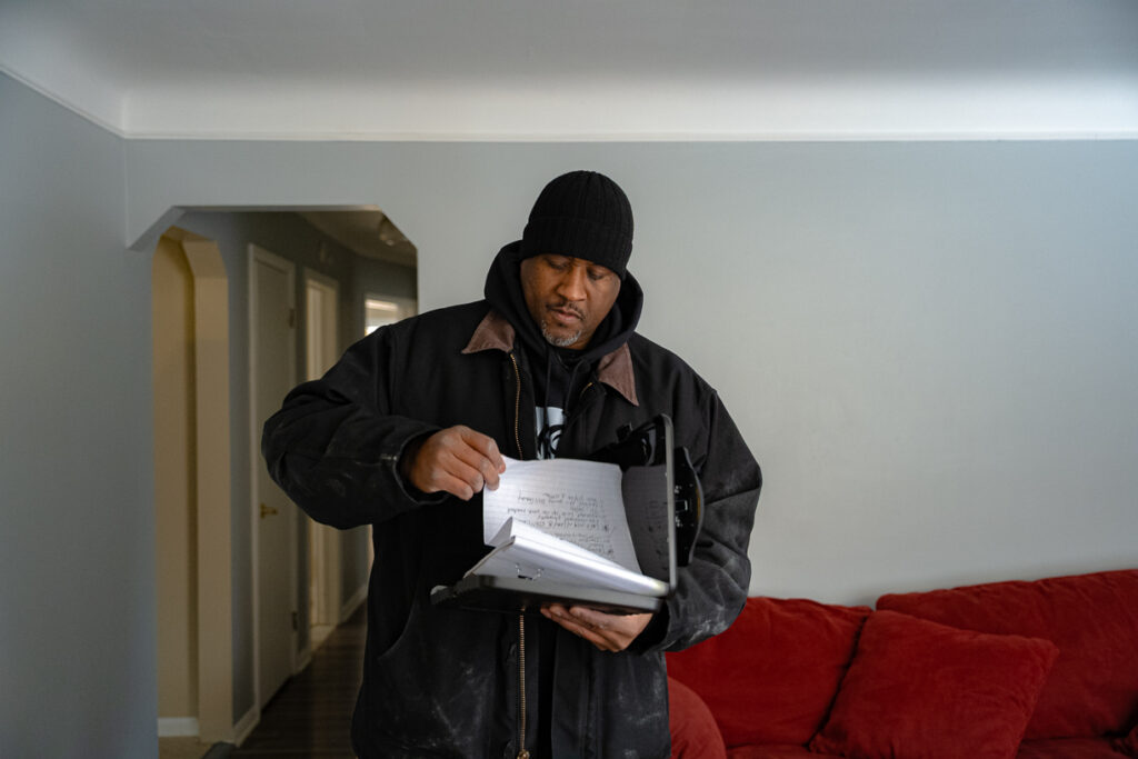 Gary Ringer reviews paperwork inside a residential home, standing near a red couch during an inspection visit.