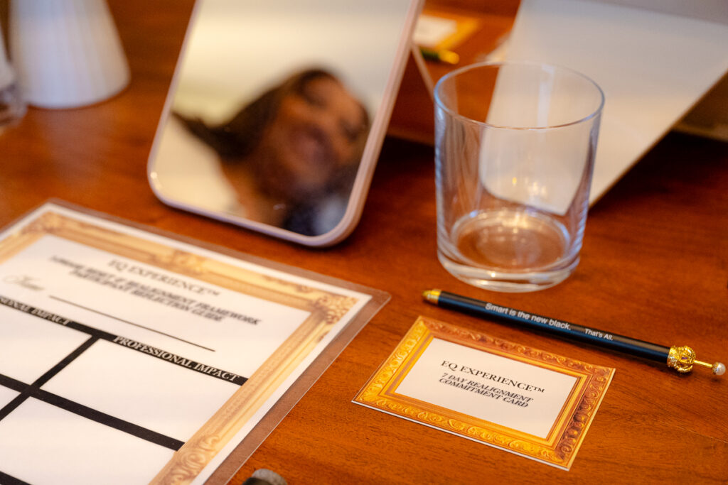 Close-up of Esthi Queen workshop materials on a table, including a mirror, glass, pen, and EQ Experience commitment cards in a wellness setting.