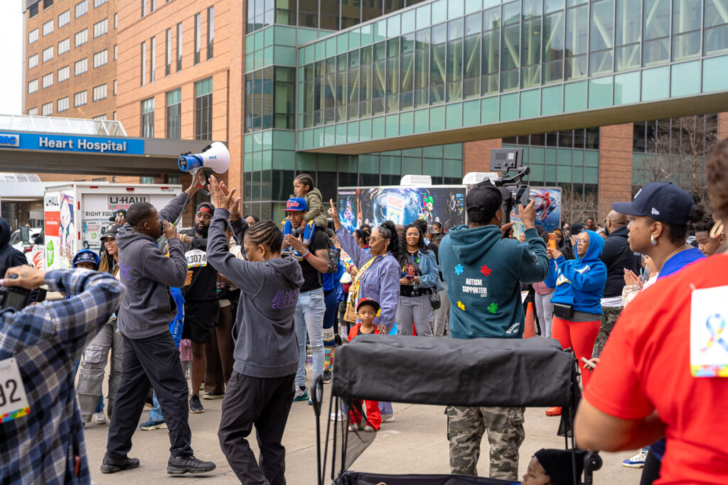 Crowd gathers outside hospital with speaker and megaphone, celebrating Autism Awareness Walk.